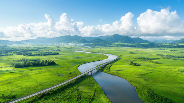 Aerial view of winding river surrounded by lush green fields and mountains bright blue sky with fluffy clouds, evoking tranquility and natural