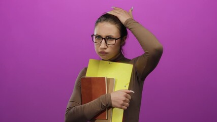 Woman expressing concern with notebooks on a pink background, wearing glasses, appears stressed and worried, isolated against a vibrant backdrop, highlighting her thoughtful mood.