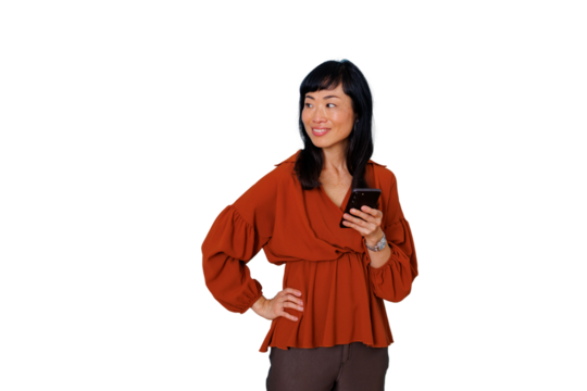 Asian executive woman smiling looking away, holding a smartphone, hand on hip, thinking about communication ideas