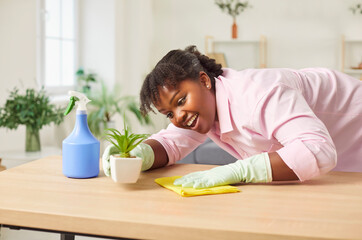 Young african american maid wiping table with yellow cloth, close-up. Female cleaner in uniform...