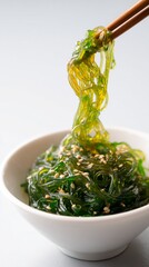 Delicately styled bowl of seaweed salad, garnished with sesame seeds, showcases vibrant green hues, perfect for healthy culinary presentations and vegan dishes.