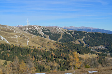 Wind turbines generating renewable energy on alpine mountains. Wind turbines standing on a partially snow-covered mountain ridge with conifer forests. Lachtal, Styria, Austria