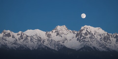 Snow covered peaks of mountain range silhouetted against deep blue sky full moon illuminating alpine terrain nighttime view