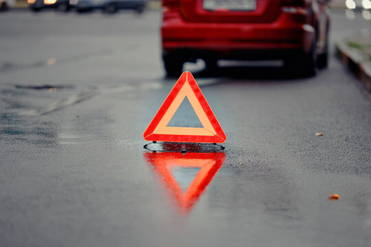 Reflective emergency triangle stands behind disabled car on rainy urban road in the evening, road safety, driver caution, and correct procedure during an unexpected breakdown situation.