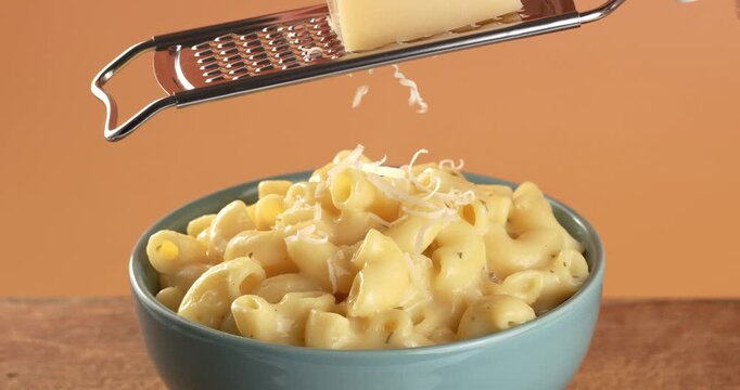 Mac and cheese in a bowl sprinkled with parmesan. Parmesan cheese being grated. Close-up footage of pasta.