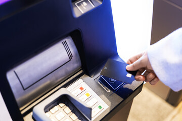 A person's hand inserting a black bank card into an ATM machine for a contactless transaction, cash withdrawal, or deposit.
