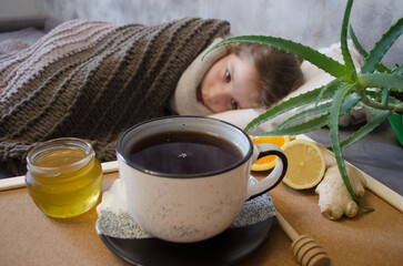 A little girl lies in bed drinking tea with lemon. Concepts of illness, cold, and acute respiratory viral infection.