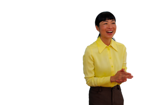 Asian woman smiling broadly and laughing, wearing a yellow shirt, hands clasped together with a transparent background