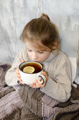 A little girl drinks tea with lemon. Concepts of illness, cold, and acute respiratory viral infection.