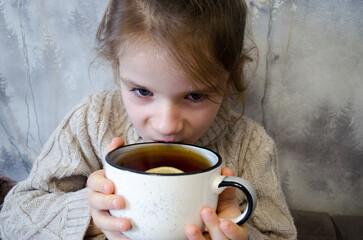 A little girl drinks tea with lemon. Concepts of illness, cold, and acute respiratory viral infection.