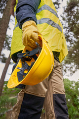 Safety equipment of an unrecognizable worker wearing reinforced clothing, reflective vest, yellow helmet and leather gloves