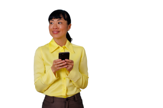 Asian businesswoman in a yellow shirt holding a smartphone, social networking or texting, smiling while looking away - Powered by Adobe