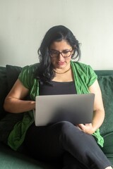 A woman is sitting on a couch and looking at a laptop
