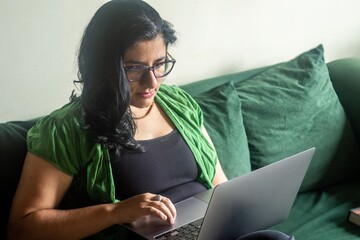 A woman is sitting on a couch and using a laptop