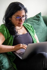 A woman is sitting on a couch and using a laptop