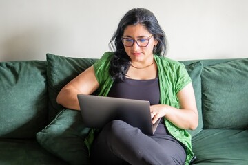 A woman is sitting on a couch and using a laptop