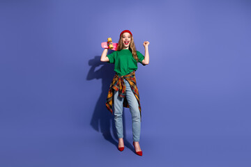 Young woman in green shirt with skateboard poses happily against a purple studio background