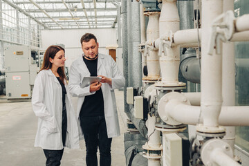 Technical team reviewing industrial systems, professionals examine piping and data collaboratively outdoors, engineering experts assess pipeline condition under natural daylight environment