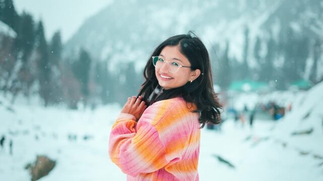 4K Portrait of beautiful Indian girl standing in snowy mountains and enjoying snowfall at Manali, Himachal Pradesh, India. Girl enjoying beautiful winter day outdoors. Tourist in winter background.