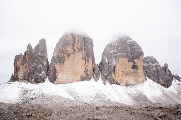 View of snow-dusted Tre Cime di Lavaredo peaks pierce the misty sky, their rugged textures contrasting with the soft white blanket, Auronzo di Cadore, Province of Belluno, Italy.