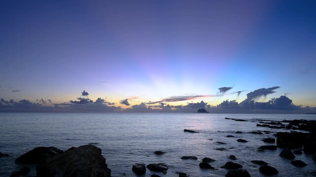 Pre-dawn in Wanli New Taipei shows orange blue sky with pink rays from horizon and drifting dark clouds over sea.