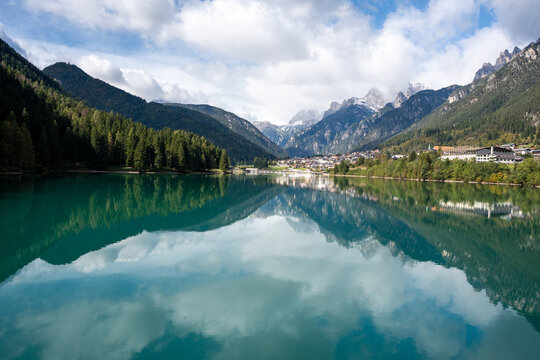 View of a serene turquoise lake mirroring the surrounding jagged mountains, lush green forests, and a quaint village, Auronzo di Cadore, Province of Belluno, Italy.
