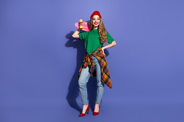 Young woman in green shirt with a skateboard on a purple background smiling in casual stylish streetwear