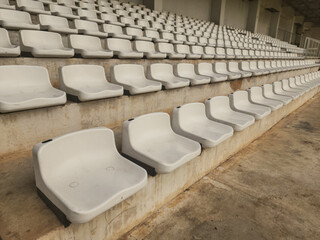 Empty white stadium seats in an outdoor sports arena, arranged in repetitive rows, emphasizing the quiet stillness of a non-event day or off-season. 