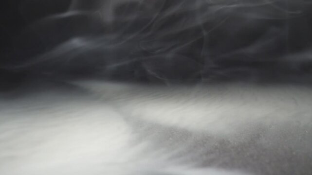 Pure club of milk steam from an electronic cigarette or hookah covering on the surface. White smoke from the vape spreading on the floor. Black background. Low view Close up Slow motion