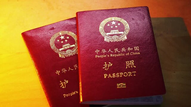 Two deep red People's Republic of China passports are stacked on wood, symbolizing Chinese international travel and border crossing.