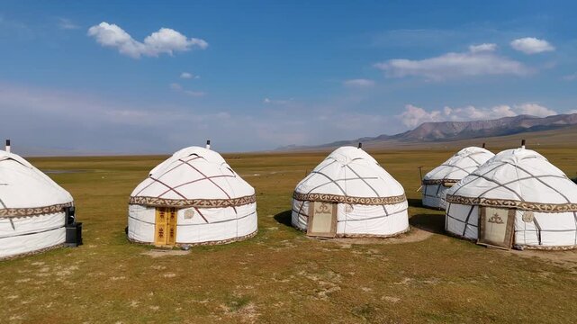 Classic Kyrgyz yurts near Song-Kul lake, standing on open grassland under a bright blue sky in a peaceful mountain setting.