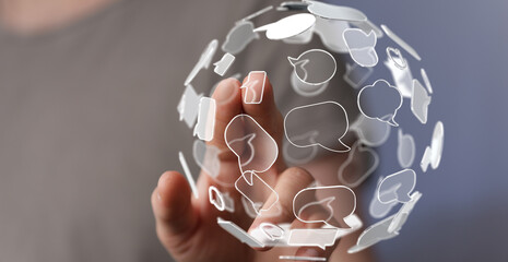 A person's hand holding a sphere made of speech bubbles, conveying communication, social media, and...