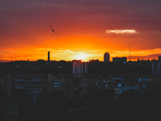 Dramatic sunset over city skyline with vibrant orange and red hues. The sun sets over the city, casting a warm glow across the buildings and sky, creating a stunning visual display