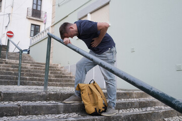 A Young Man Having a Heart Attack on the Street, Standing on the Stairs and Holding His Chest 