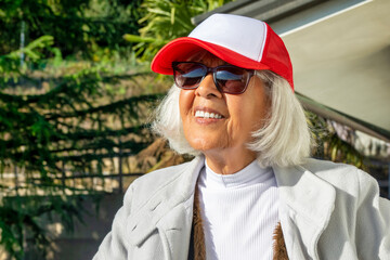Smiling senior woman wearing sunglasses and red cap outdoors on a sunny day