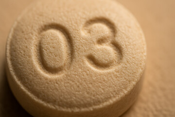 A detailed macro photo of a beige tablet featuring engraved numbers, showcasing the pill’s texture, manufacturing precision, and pharmaceutical identification marks.