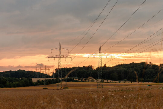 High-voltage power lines crossing fields at sunset with dramatic clouds and warm evening light.