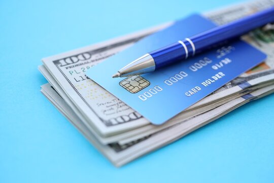 Credit card and pen with US dollar currency money bills banknotes on light blue background. Business, financial operations and accounting in United States of America