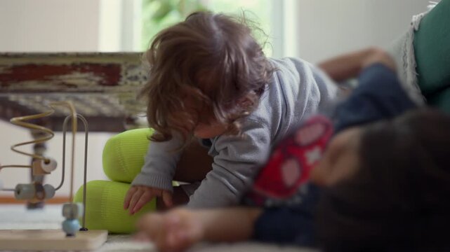 Toddler climbing onto older brother during playful wrestling on living room carpet beside teal sofa, energetic sibling play