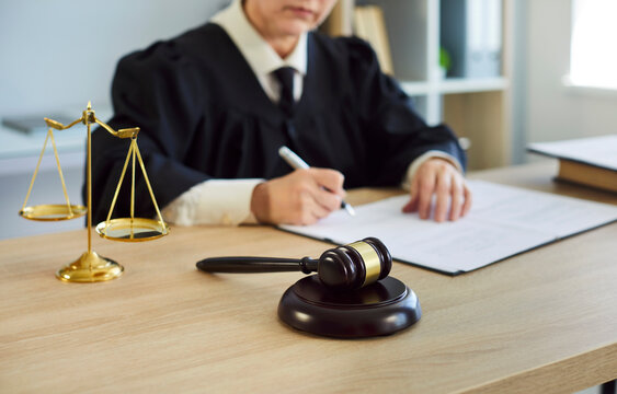 Woman judge signs legal document in courtroom. Symbol of justice and law, gavel on desk as official writes ruling in judicial robe, in bright office with files. Jurisdiction concept.
