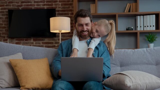 Happy Caucasian family at home cute daughter hugging father working with laptop smiling together childcare carefree child kid girl cuddling embracing hug daddy distract from online work with computer