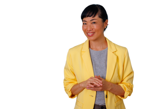 Asian woman in a yellow blazer and grey t-shirt smiling, looking at the camera with her hands clasped, transparent background