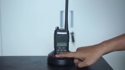 Hand adjusting a two-way radio walkie-talkie on a charger, showcasing its antenna, buttons, and LCD display. Ideal for security, construction, and emergency communication stock footage.