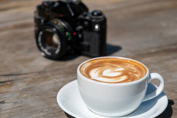 Latte coffee and camera on wooden table. Warm latte and vintage camera still life. Photographer’s coffee break with latte and camera.
