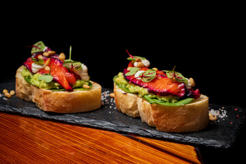 Delicious avocado toast garnished with roasted vegetables and fresh herbs sits on a stylish slate
