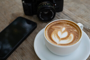 Creative workspace with coffee, camera, and phone. Latte coffee with camera and smartphone on wooden table. Coffee break with camera and mobile phone.