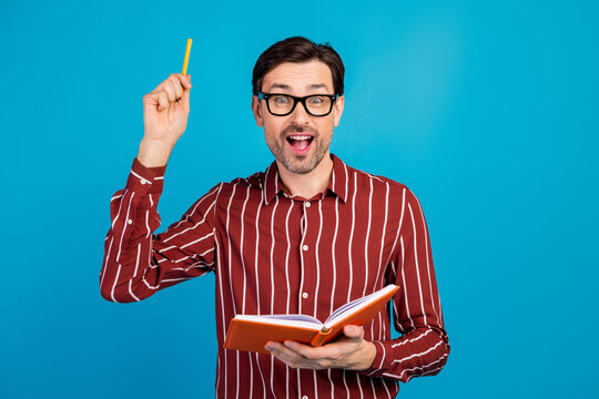 Young stylish man with glasses holds notebook and pencil smiling against blue background - Powered by Adobe