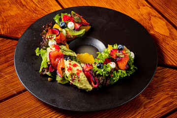 Colorful seafood salad artfully presented on a dark plate, fresh and tempting, surrounded by greens
