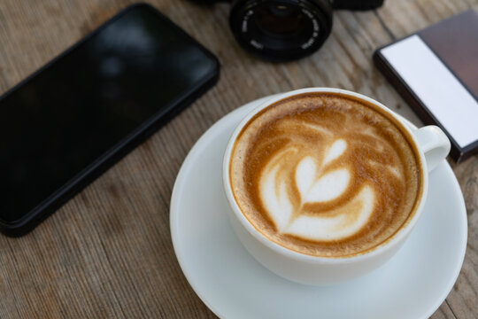 Creative workspace with coffee, camera, and phone. Latte coffee with camera and smartphone on wooden table. Coffee break with camera and mobile phone.