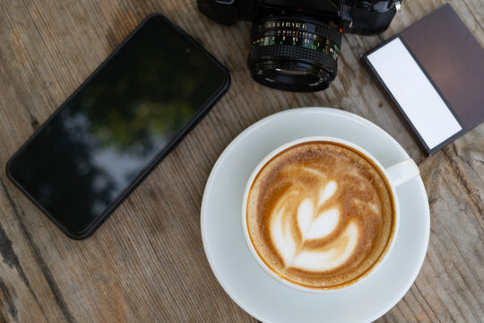 Creative workspace with coffee, camera, and phone. Latte coffee with camera and smartphone on wooden table. Coffee break with camera and mobile phone.